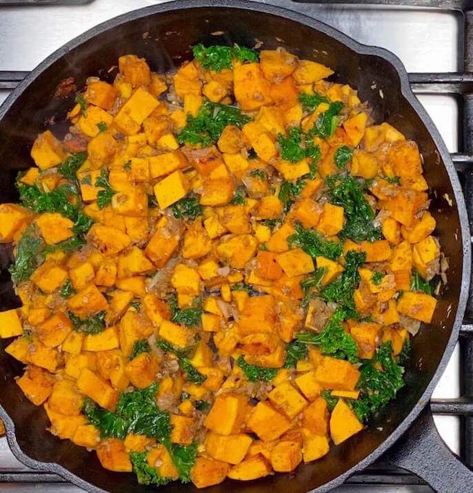 Cast Iron Skillet with Cooked Sweet Potatoes, Diced White Onion,Garlic, Cinnamon, and Kale | Kale Sweet Potato Hash | The Radiant Root