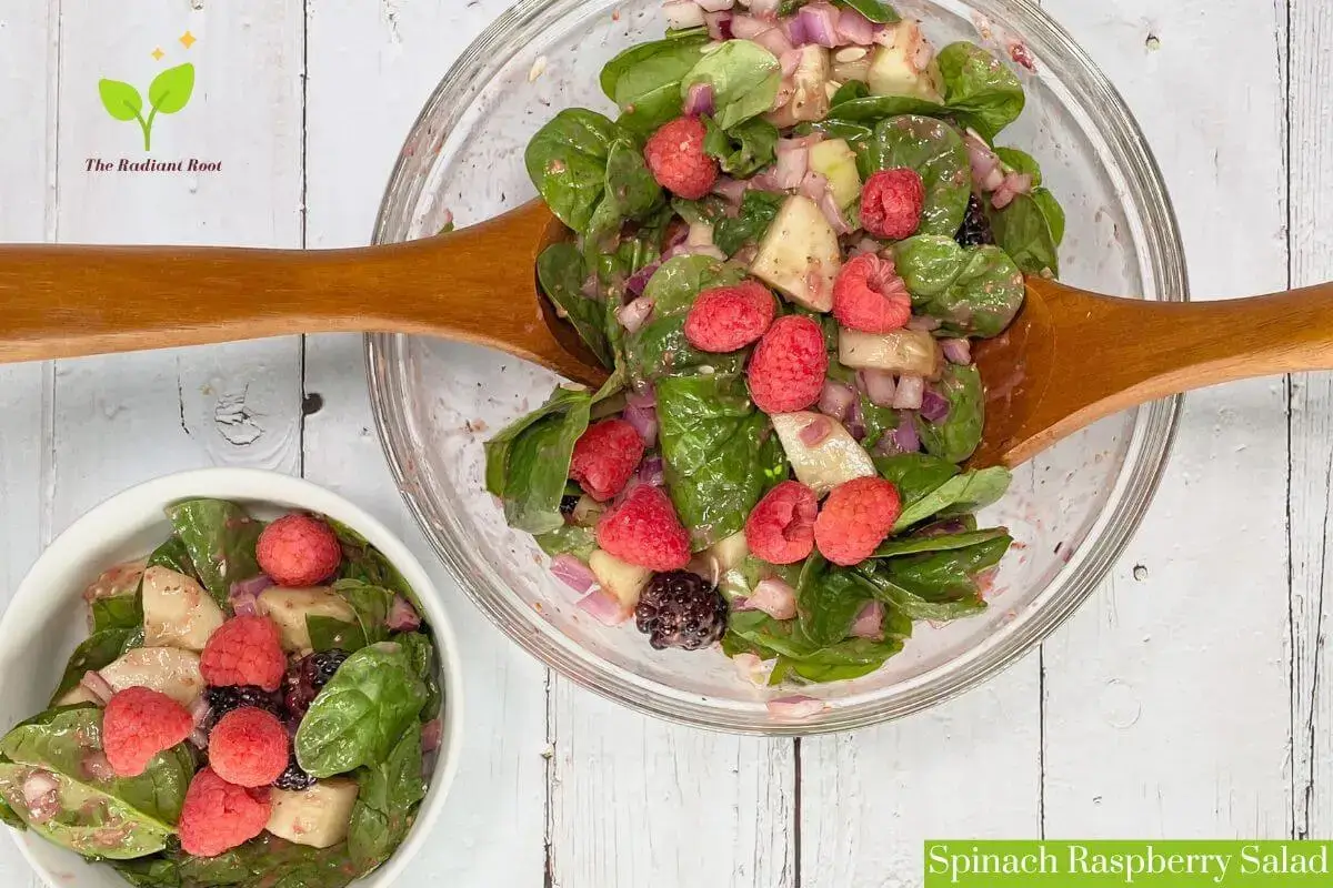 Spinach Raspberry Salad a spinach salad in a glass bowl with raspberry balsamic vinaigrette on a white wooden table | The Radiant Root
