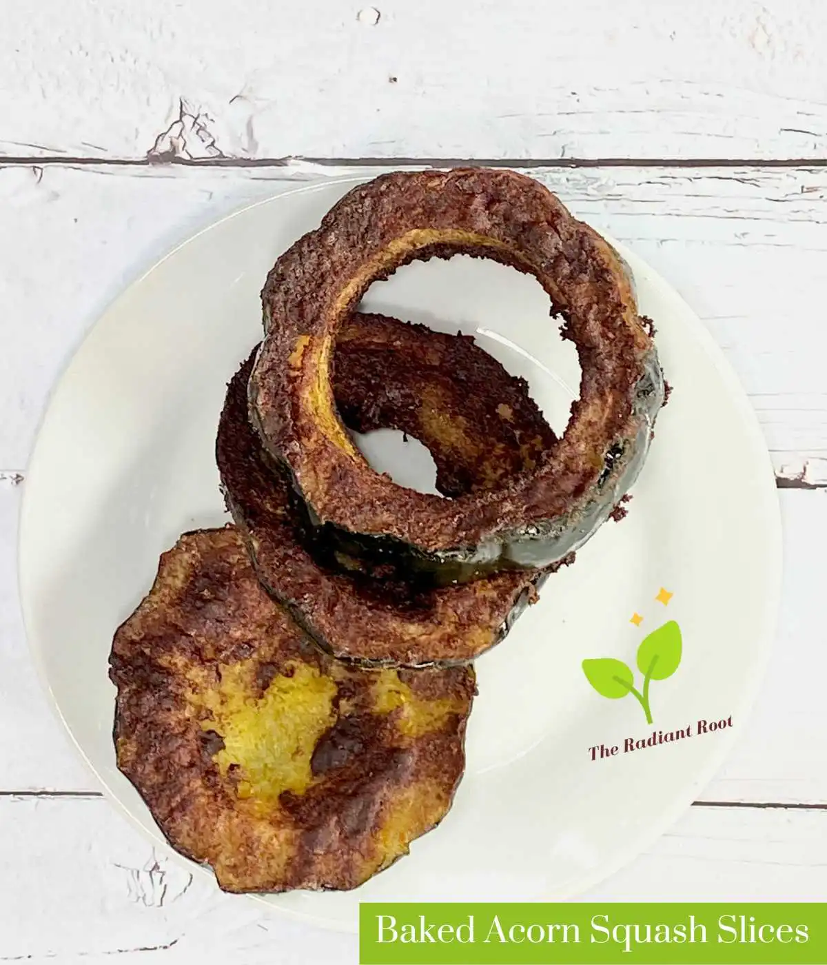 A white wooden table with a white plate with cooked acorn squash rings and the words “Baked Acorn Squash Slices.” | Baked Acorn Squash Slices | The Radiant Root