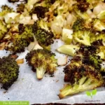 A close of up finished recipe of the balsamic roasted broccoli on a baking sheet with the words "The Radiant Root" in white font with green outline | Roasted Balsamic Broccoli | The Radiant Root