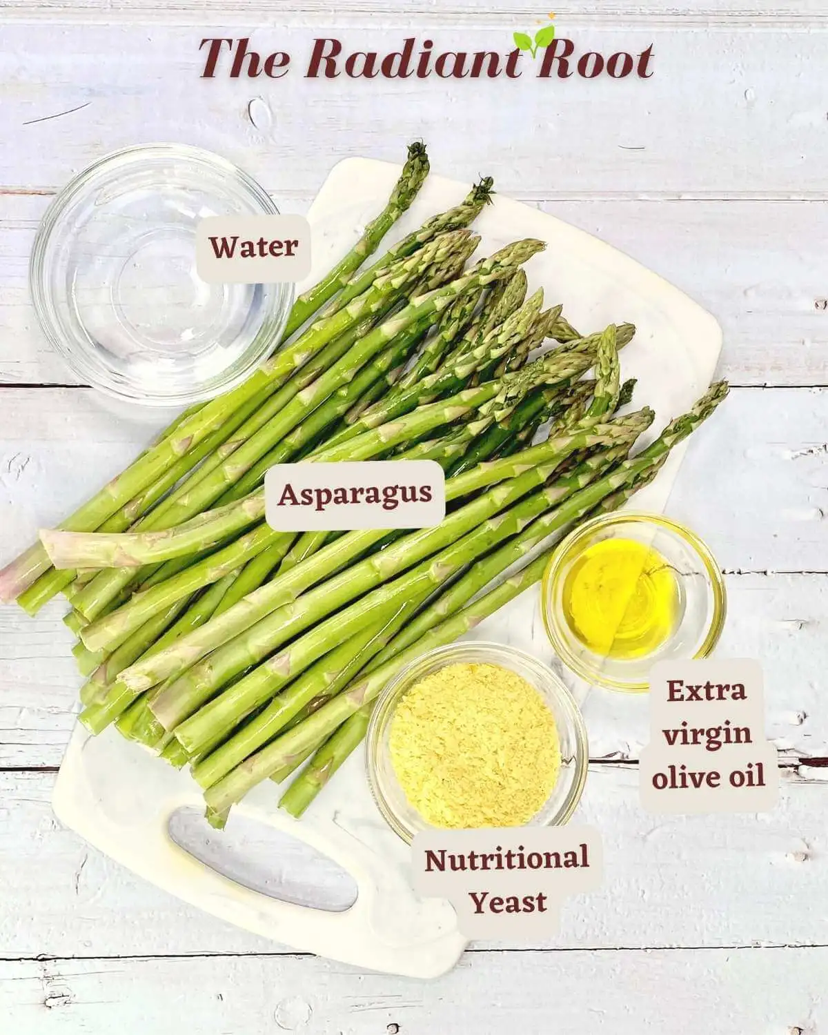A white wooden table with a cutting board. At the top is reads “The Radiant Root.” On the table sits a pound of asparagus and three small clear mixing glasses holding the other ingredients: nutritional yeast, water, and extra virgin olive oil. | cheesy” asparagus recipe | The Radiant Root