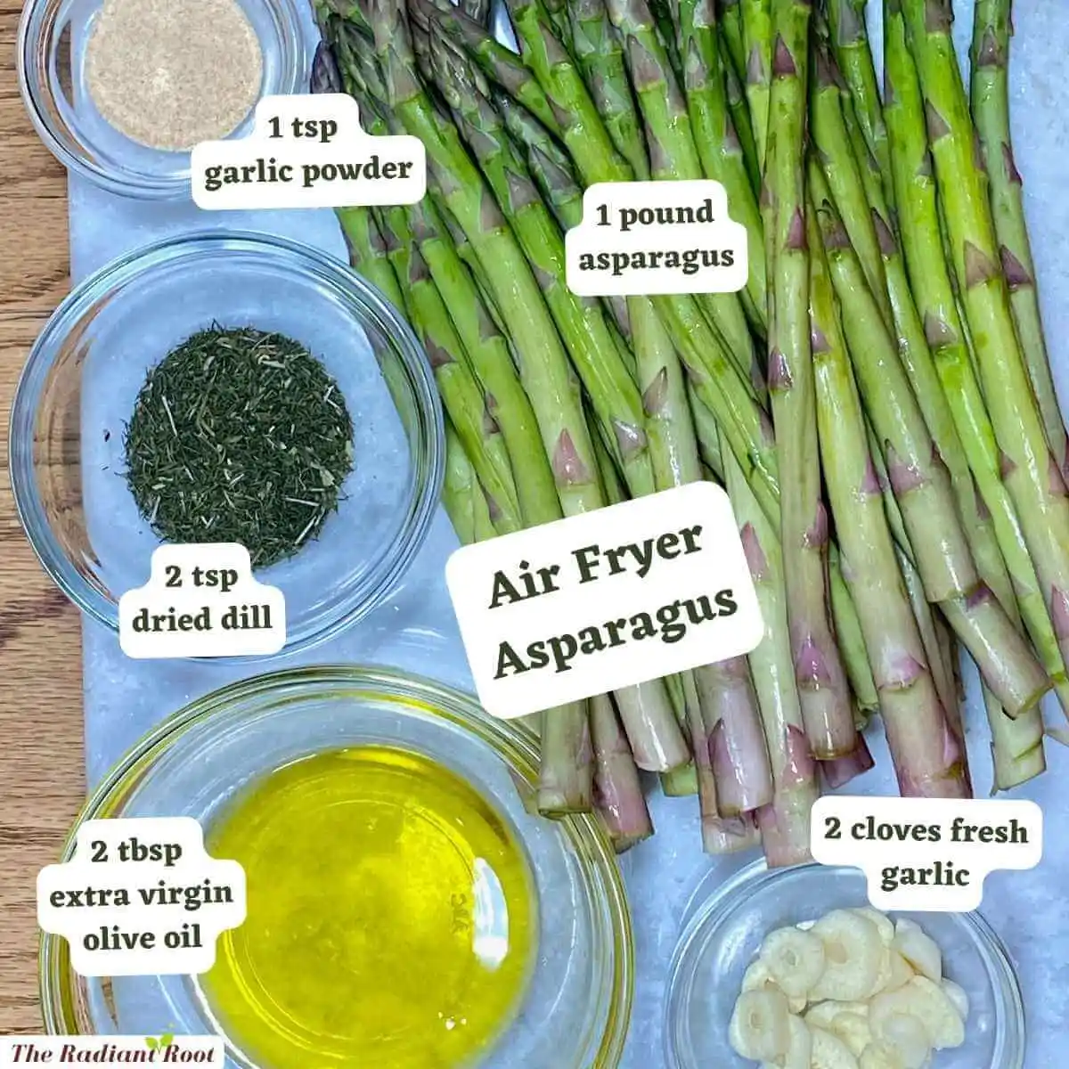 Ingredient Photo: A wooden table with a blue cutting board. On top of the cutting board are the ingredients for this recipe: asparagus and in small clear glass bowls are the other ingredients garlic powder, dried dill, extra virgin olive oil, and fresh garlic. The words read “Air Fryer Asparagus.” Then next to each ingredient it reads what it is “1 tsp garlic powder,” “1 pound asparagus,” “2 tsp dried dill,” 2 tbsp extra virgin olive oil,” and “2 cloves fresh garlic.” | fried asparagus recipe | The Radiant Root