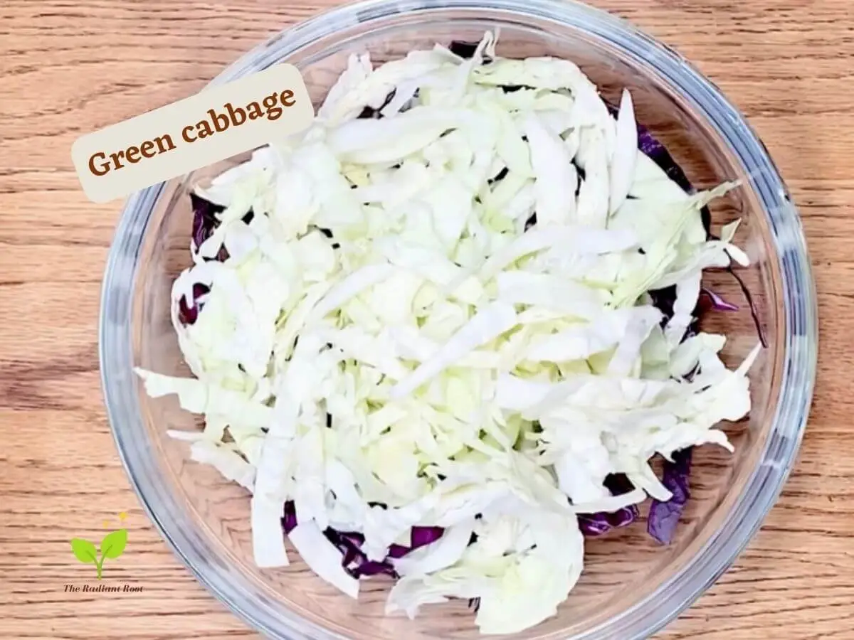 Whole30 coleslaw recipe photo 2 of 8: A wooden table with a large clear glass bowl containing shredded purple cabbage and shredded green cabbage. It reads “green cabbage.” | best ever coleslaw recipe | The Radiant Root