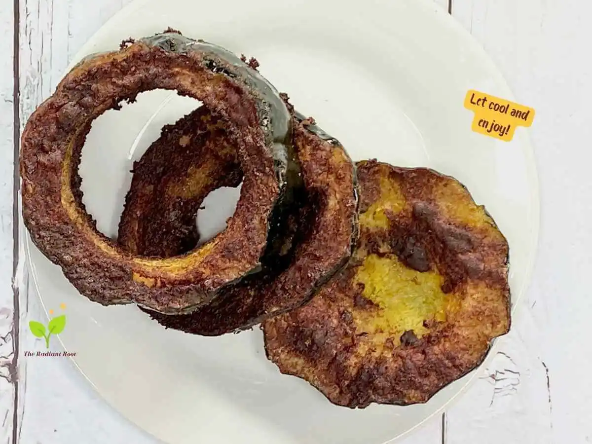 Instructions 19 of 19 for the baked acorn squash slices: A photo of a white woodent table with a white plate. One top of the plate is the cooked acorn squash and the words “let cool and enjoy.” | Baked Acorn Squash Slices | The Radiant Root