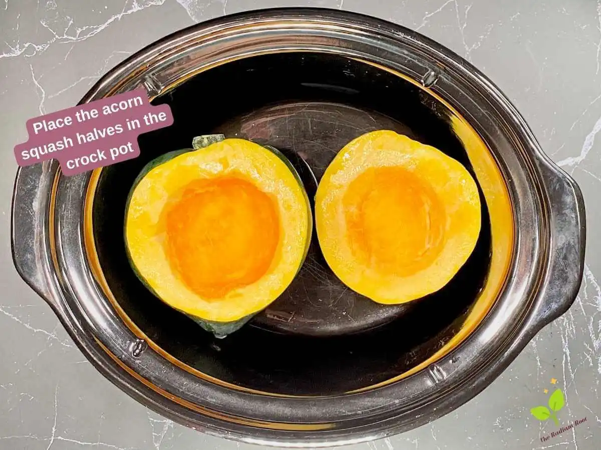 Instruction 5 of 10 for the crock pot acorn squash: A grey slab background with a black crock pot containg two acorn squash halves in it. In the top left corner words say “Place the acorn squash halves in the crock pot.” | Crock Pot Acorn Squash | The Radiant Root