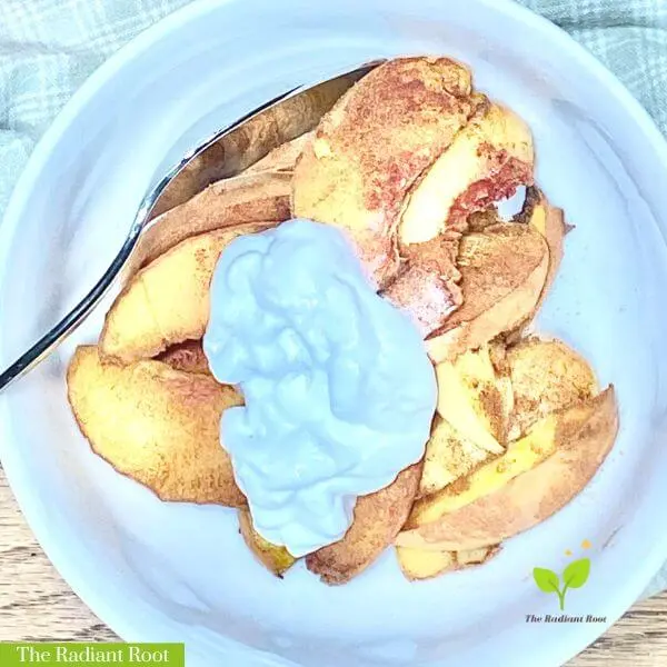 Air Fryer Peaches topped with coconut cream in a white bowl on a blue checked towel | Air Fryer Peaches | The Radiant Root