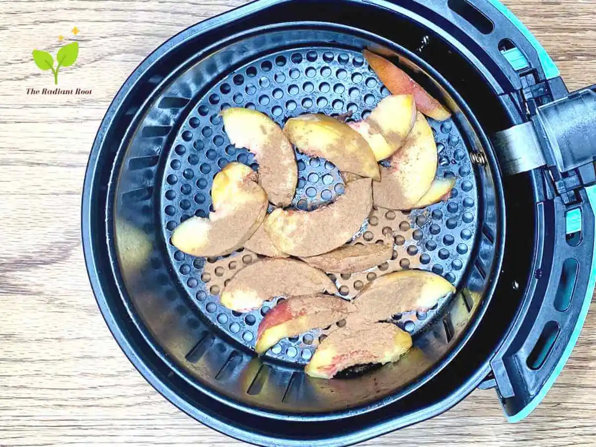 Air Fryer Peaches recipe ingredient step photo 2 of 3 with an air fryer basked with a peach raw and sliced laid out in the air fryer basket | The Radiant Root