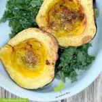 acorn squash air fryer with olive oil, garlic, and thyme in a white bowl surrounded by a bed of kale on a brown wooden table | The Radiant Root