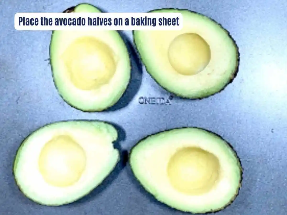 Avocado Egg Boats Instruction photos 5 of 8: A wooden table with a baking sheet containing four avocado halves pitted next to each other | bake an egg in an avocado. It reads “place the avocado halves on a baking sheet.”| The Radiant Root