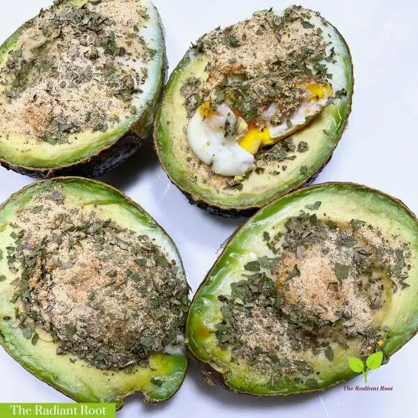 A white plate with avocados filled with eggs and spices and a sign that says Avocado Egg Boats Recipe | The Radiant Root