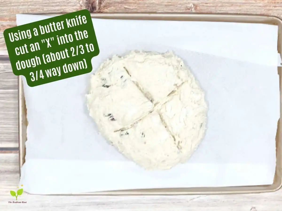 Gluten Free Irish Soda Bread Instruction 11 of 14: Raw Irish soda bread dough with an “X” cut into the middle. It reads in dark green “using a butter knife cut an X into the dough (about 2/3 to 3/4 way down).” | Gluten Free Irish Soda Bread | The Radiant Root