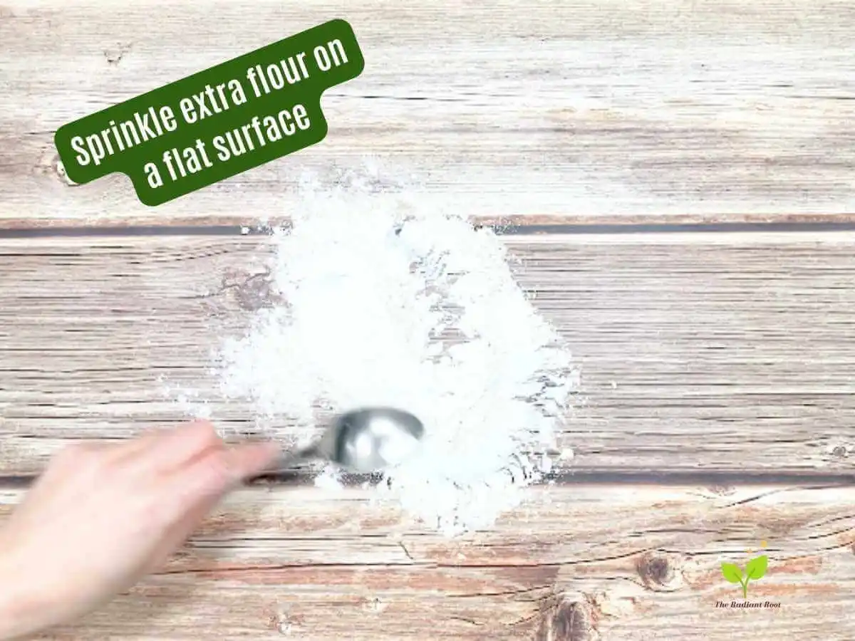 Gluten Free Irish Soda Bread Instruction 7 of 14: A brown wooden table with white gluten free flour sprinkled on top and the words read “sprinkle extra flour on a flat surface.” | Gluten Free Irish Soda Bread | The Radiant Root