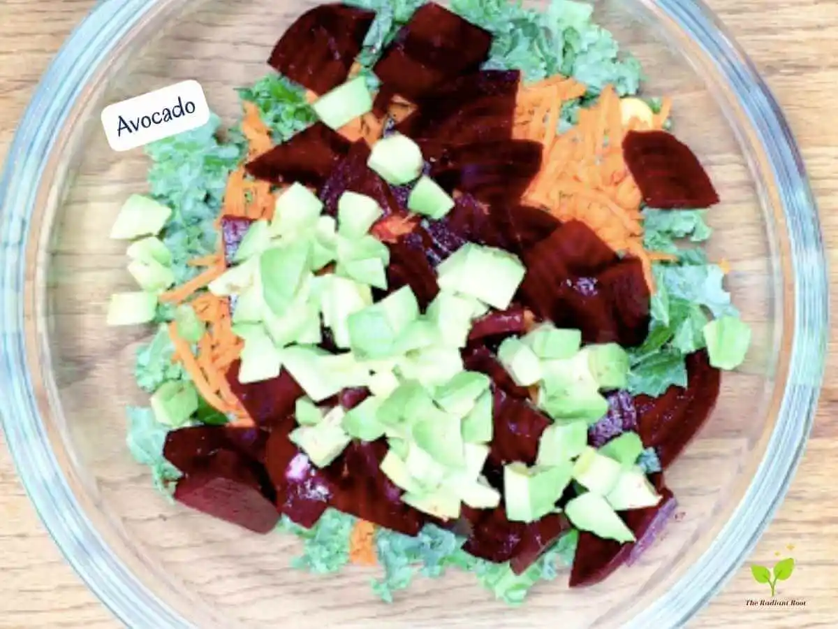 Lupini beans salad photo 12 of 15 : A wooden table with a large clear glass bowl containing the salad ingredients: kale, lupini beans, shredded carrots, roasted beets, and avocado. It reads “avocado.” | lupini bean recipe | The Radiant Root