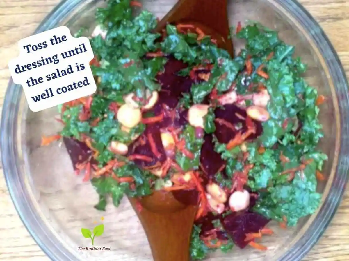 Lupini beans salad photo 14 of 15 : A wooden table with a large clear glass bowl containing the salad ingredients: kale, lupini beans, shredded carrots, roasted beets, and avocado tossed with salad dressing containing salad tongs inside the bowl. It reads “toss the dressing until the salad is well coated.” | lupini beans | The Radiant Root