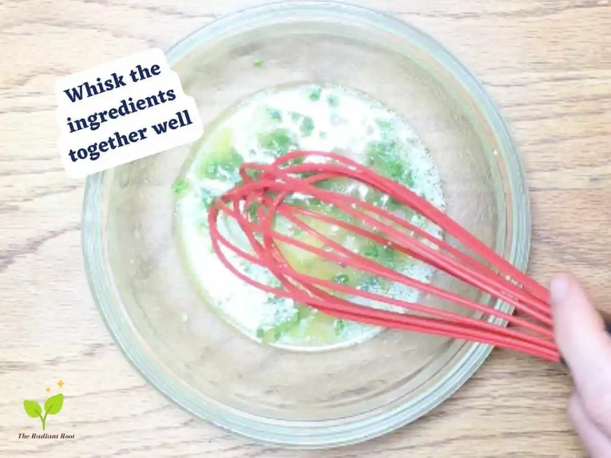 Lupini beans salad photo 7 of 15 : A wooden table with a clear glass bowl containing olive oil, diced shallots, dry mustard, fresh parsley, and lemon zest mixed together. A red whisk is sitting in the bowl. It reads “whisk the ingredients together well.” | Lupini beans benefits | The Radiant Root