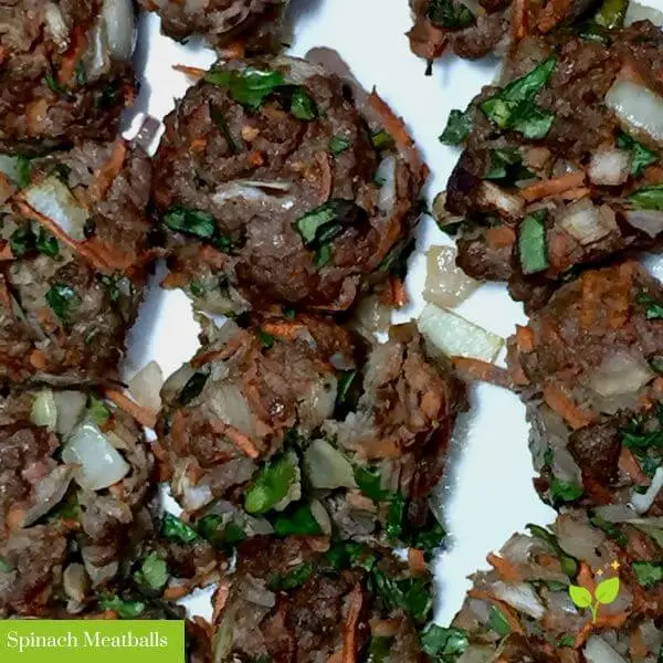 A close up photo of a white plate containing cooked spinach meatballs containing grass-fed beef, shredded carrots, chopped spinach, white onion, oregano, and basil. Below there is a green border that says “The Radiant Root” | how to make meatballs easy | The Radiant Root