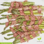 Oven roasted asparagus spears wrapped in turkey bacon in a pile on a white plate | Asparagus Wrapped In Turkey Bacon | The Radiant Root