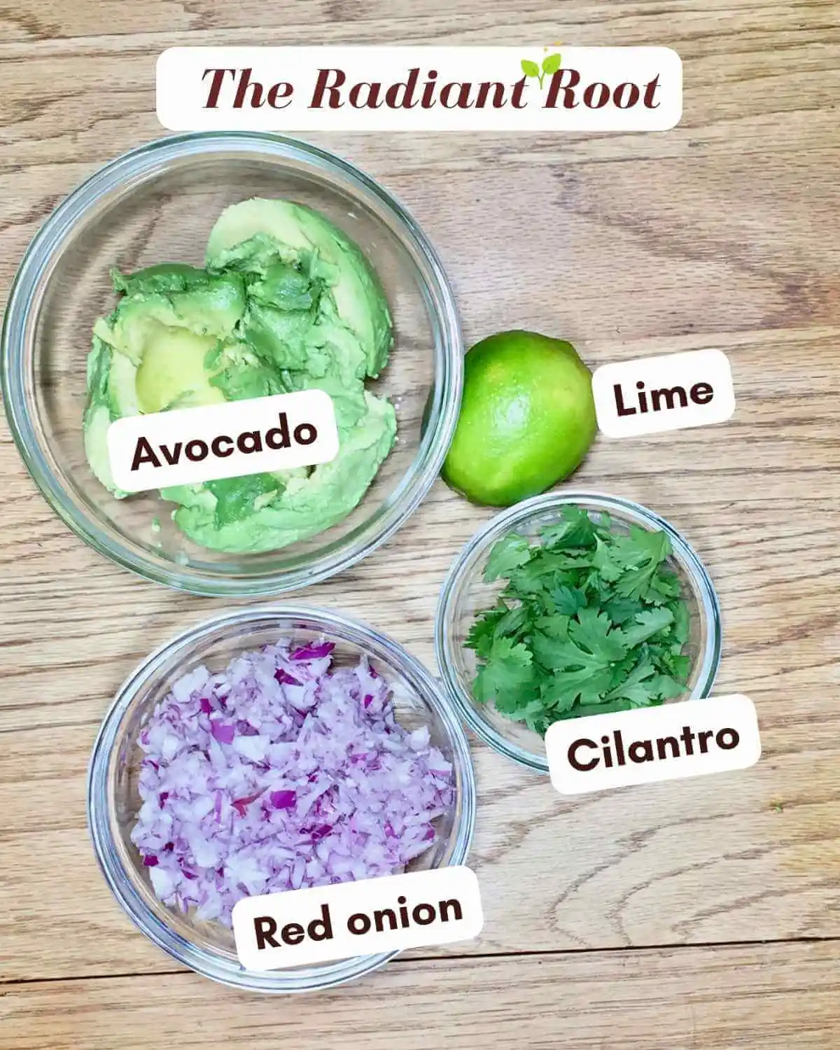 Food Processor Guacamole: At the top it reads “The Radiant Root.” There is a wooden table with small clear glass bowls containing the ingredients for food processor guacamole avocados, a lime, red onion, and cilantro with the names of the ingredients next to them. | Ingredients for guacamole | The Radiant Root