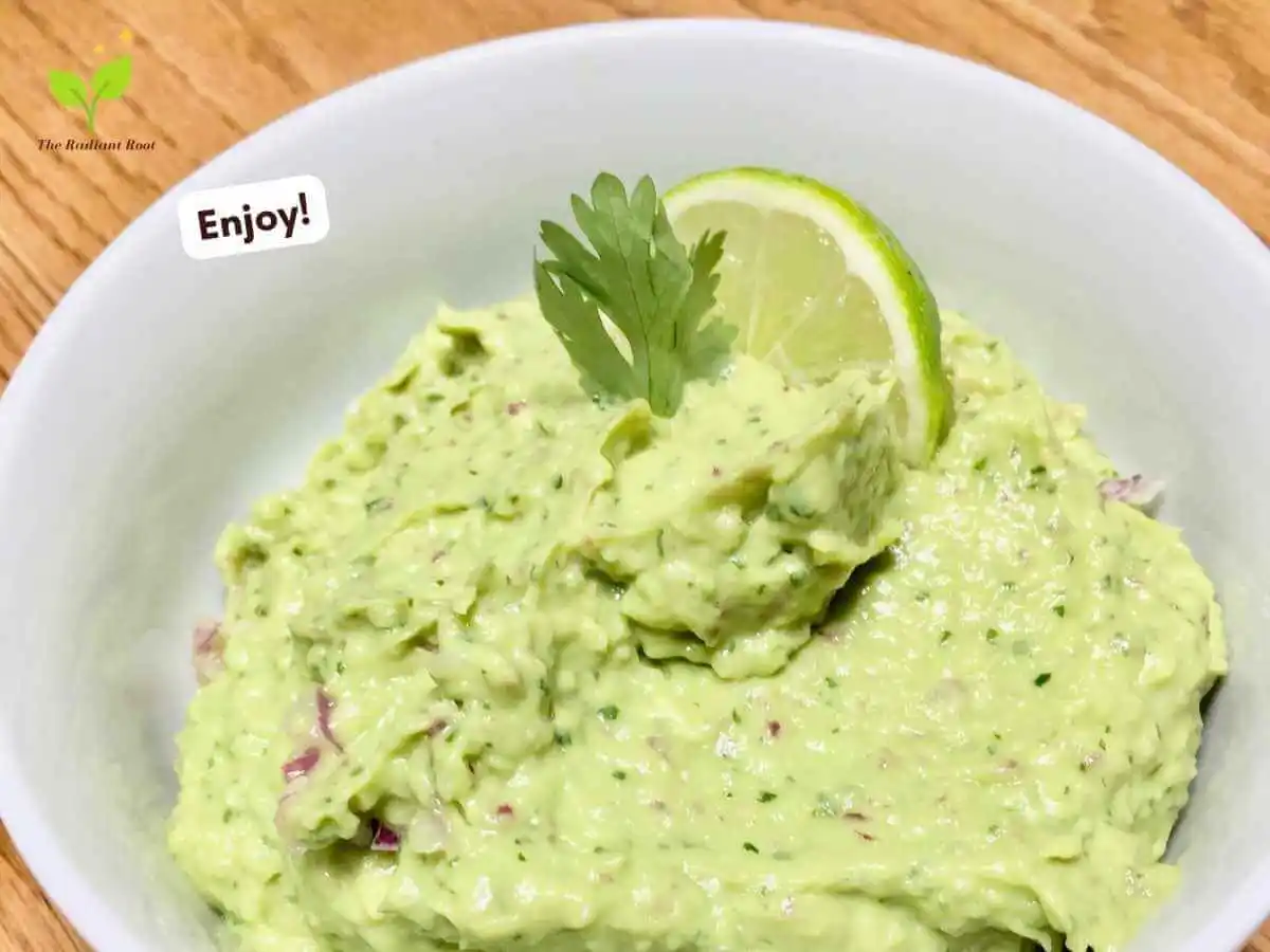 Food Processor Guacamole recipe instruction photo 7 of 7 : There is a close up of a wooden table containing the finished guacamole with a lime and cilantro leaf sticking out of it sitting on wooden table. In the lower left corner it reads “enjoy.” | fresh guacamole recipe | The Radiant Root