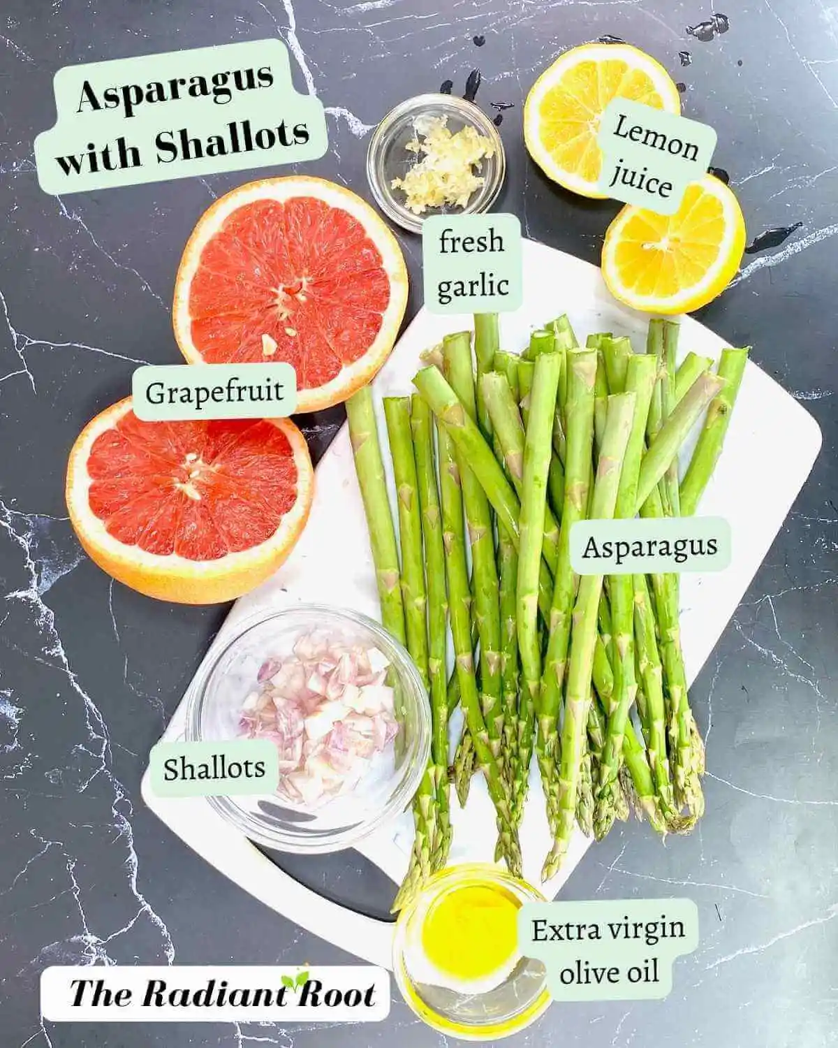 Asparagus with Shallots Ingredient photo: A black marble counter top with the ingredients for the asparagus and shallot recipe. There is a cutting board containing trmmed asparagus. Next to that is a bowl of peeled and diced shallots. To the bottom of that is a small clear glass dish with extra virgin olive oil. Next to the cutting board there is a grapefruit cut in half. Next to that on the rigth is a small clear glass dish with the peeled and pressed fresh garlic. Next to that on the right is a lemon cut in half. Next to each ingredient it reads the ingredient’s name. | shallot recipe | The Radiant Root