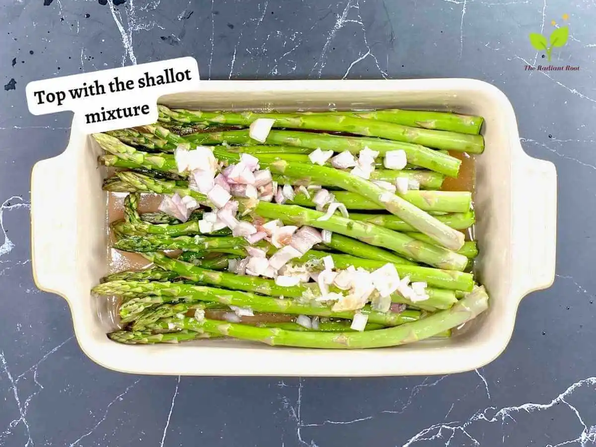 Asparagus with Shallots 10 of 12 : A black marble counter top with a baking dish 7 x 10 inches containing the raw asparagus topped with the shallot marinade mixture. It reads “top with the shallot mixture.” | How to cut a shallot | The Radiant Root