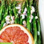 Asparagus with Shallots WP Recipe Photo: Close up photo of roasted asparagus with shallots in a white dish topped with a marinade of grapefruit juice, lemon juice, shallots, garlic, and extra virgin olive oil, topped with a grapefruit slice garnish. In the bottom left corner it reads “The Radiant Root.” | What are shallots | The Radiant Root