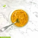 Cauliflower Butternut Squash Mash WP Recipe Photo: A close up of the finished cauliflower butternut squash mash in a white bowl with a silver spoon. In the bottom left corner it reads “The Radiant Root.” | mashed cauliflower and butternut squash | The Radiant Root