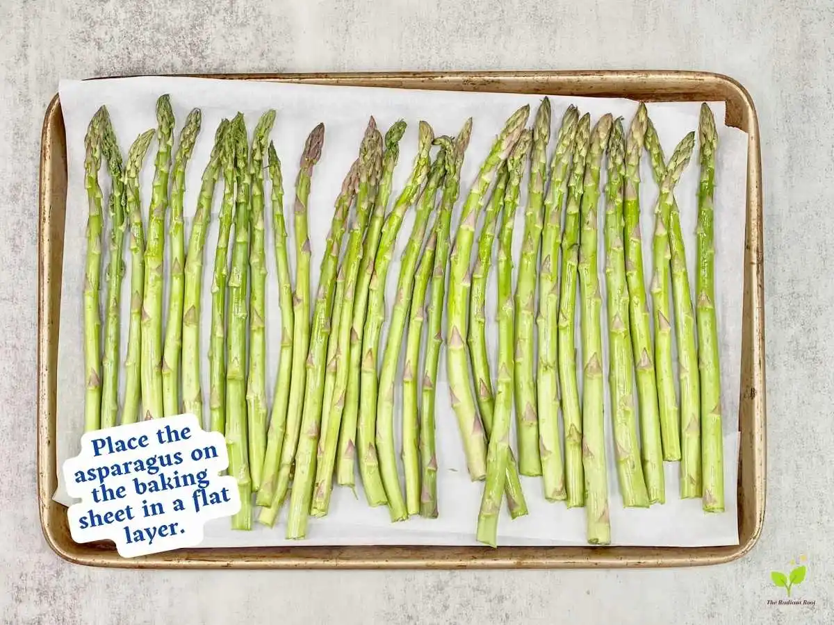 Balsamic glazed asparagus recipe instruction photo 7 of 10 : A grey marble table top containing a lined baking sheet containing of fresh raw asparagus in a flat layer. It reads “place the asparagus on the baking sheet in a flat layer.” | what does balsamic vinegar taste like | The Radiant Root