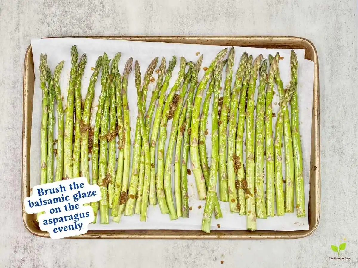 Balsamic glazed asparagus recipe instruction photo 8 of 10 : A grey marble table top containing a lined baking sheet containing of fresh raw asparagus in a flat layer. The asparagus is coated with balsamic glaze. It reads “brush the balsamic glaze on the asparagus evenly.” | balsamic vinegar taste | The Radiant Root