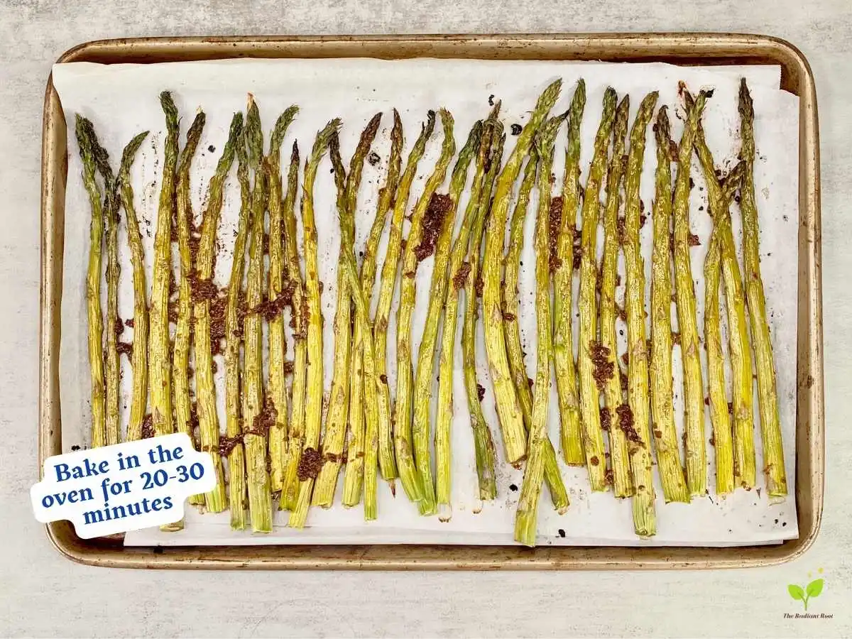 Balsamic glazed asparagus recipe instruction photo 9 of 10 : A grey marble table top containing a lined baking sheet containing of the cooked balsamic glazed asparagus. It reads “bake in the oven for 20 to 30 minutes.” | balsamic vinegar nutrition | The Radiant Root