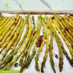 Balsamic glazed asparagus WP Recipe Photo: A close up of a baking sheet with parchment paper containing finished roasted asparagus roasted with baslamic glaze behind it is a marblized wall. | best roasted asparagus | The Radiant Root