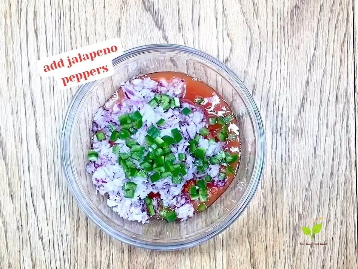 Cilantro salsa recipe instruction photo 3 of 8: A close-up of a wooden table containing a medium glass mixing bowl containing diced canned tomatoes, diced red onion, and diced jalapeno peppers. It reads “Add jalapeno peppers.” | easy fresh salsa recipe | The Radiant Root