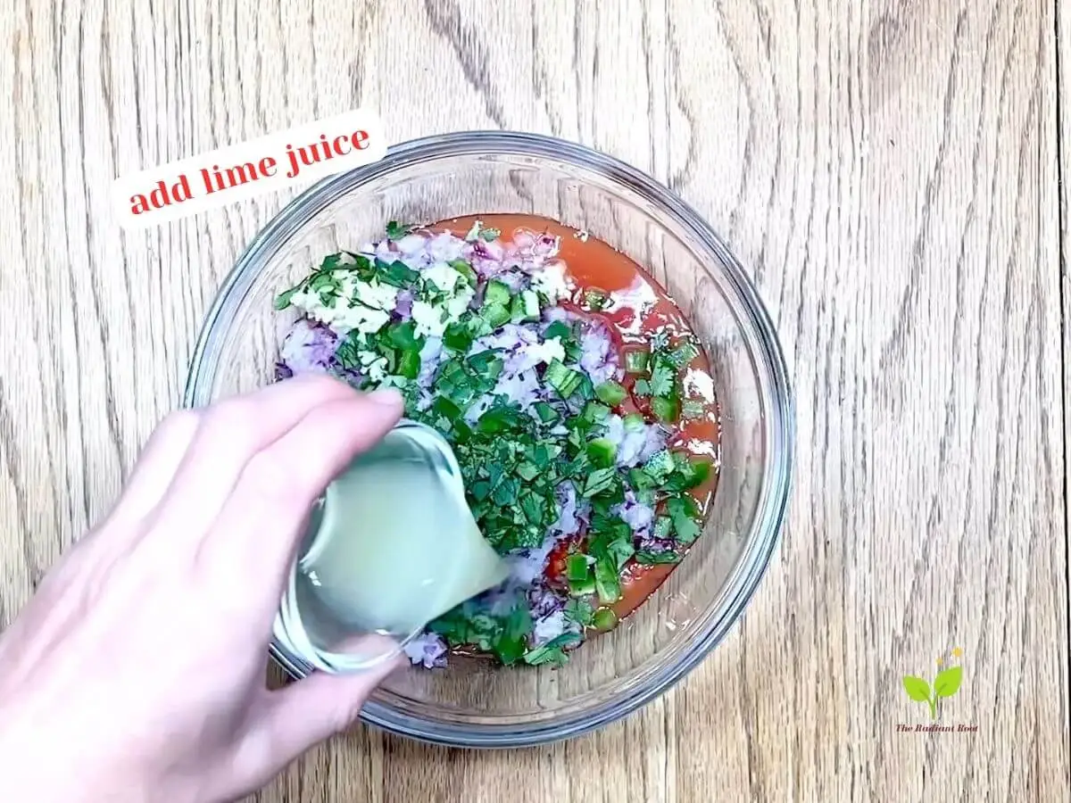 Cilantro salsa recipe instruction photo 6 of 8: A close-up of a wooden table containing a medium glass mixing bowl containing diced canned tomatoes, diced red onion, diced jalapeno peppers, cilantro, garlic, and a hand-pouring lime juice into the bowl. It reads “Add lime juice.” | homemade cilantro salsa | The Radiant Root