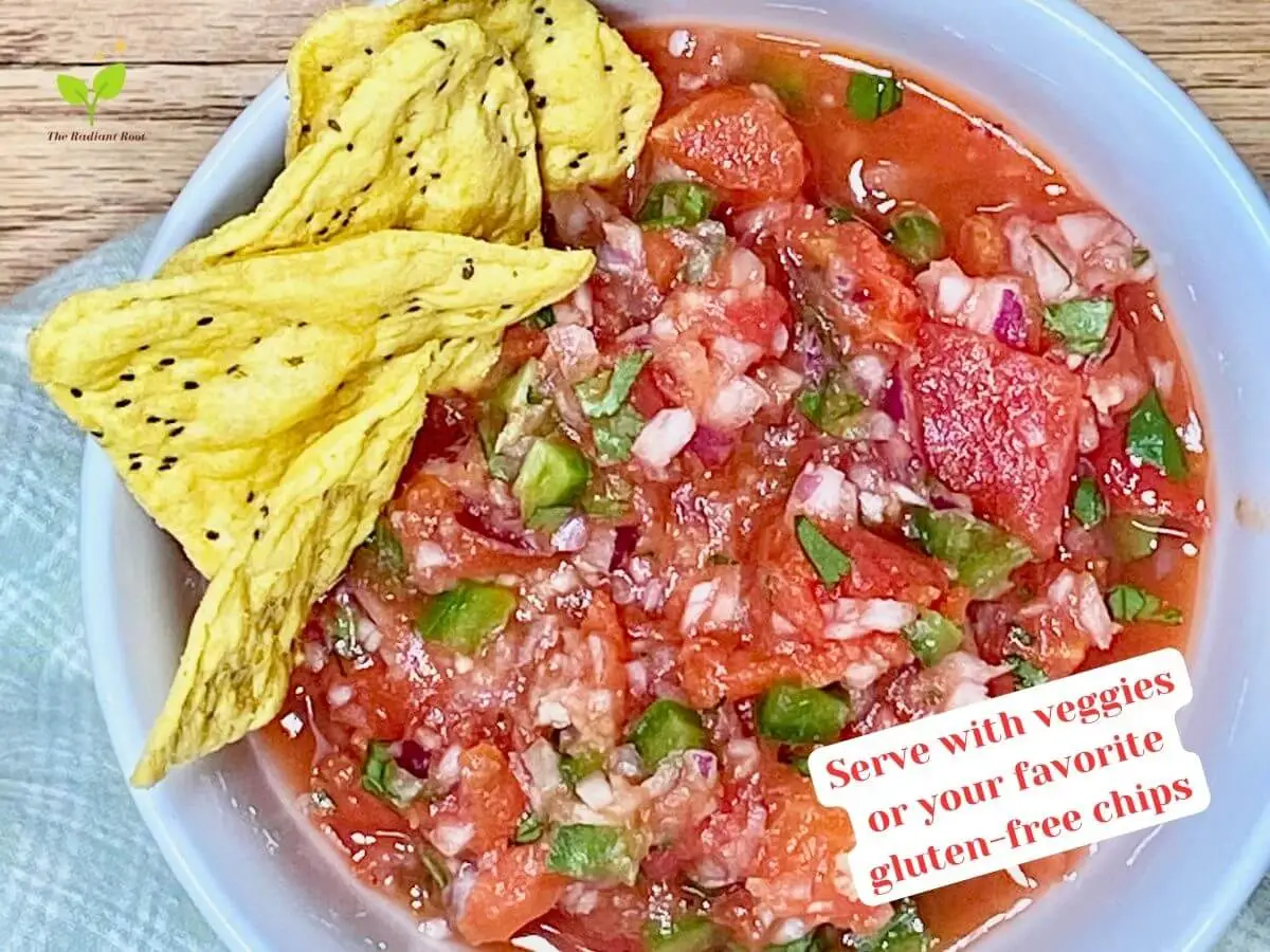 Cilantro salsa recipe instruction photo 8 of 8: A close-up of a wooden table containing a white bowl with the finished salsa consisting of diced canned tomatoes, diced red onion, diced jalapeno peppers, cilantro, garlic, and lime juice. In the bowl sticking out are gluten-free tortilla chips. It reads “Serve with veggies or your favorite gluten-free chips.” | recipe for salsa | The Radiant Root