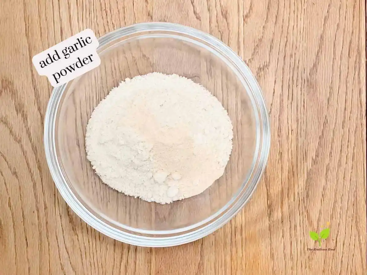 GF Chicken Wings recipe instruction photo 5 of 14 : A wooden table containing a large mixing bowl containing almond flour and garlic powder. It reads “add garlic powder.” | What is almond flour | The Radiant Root