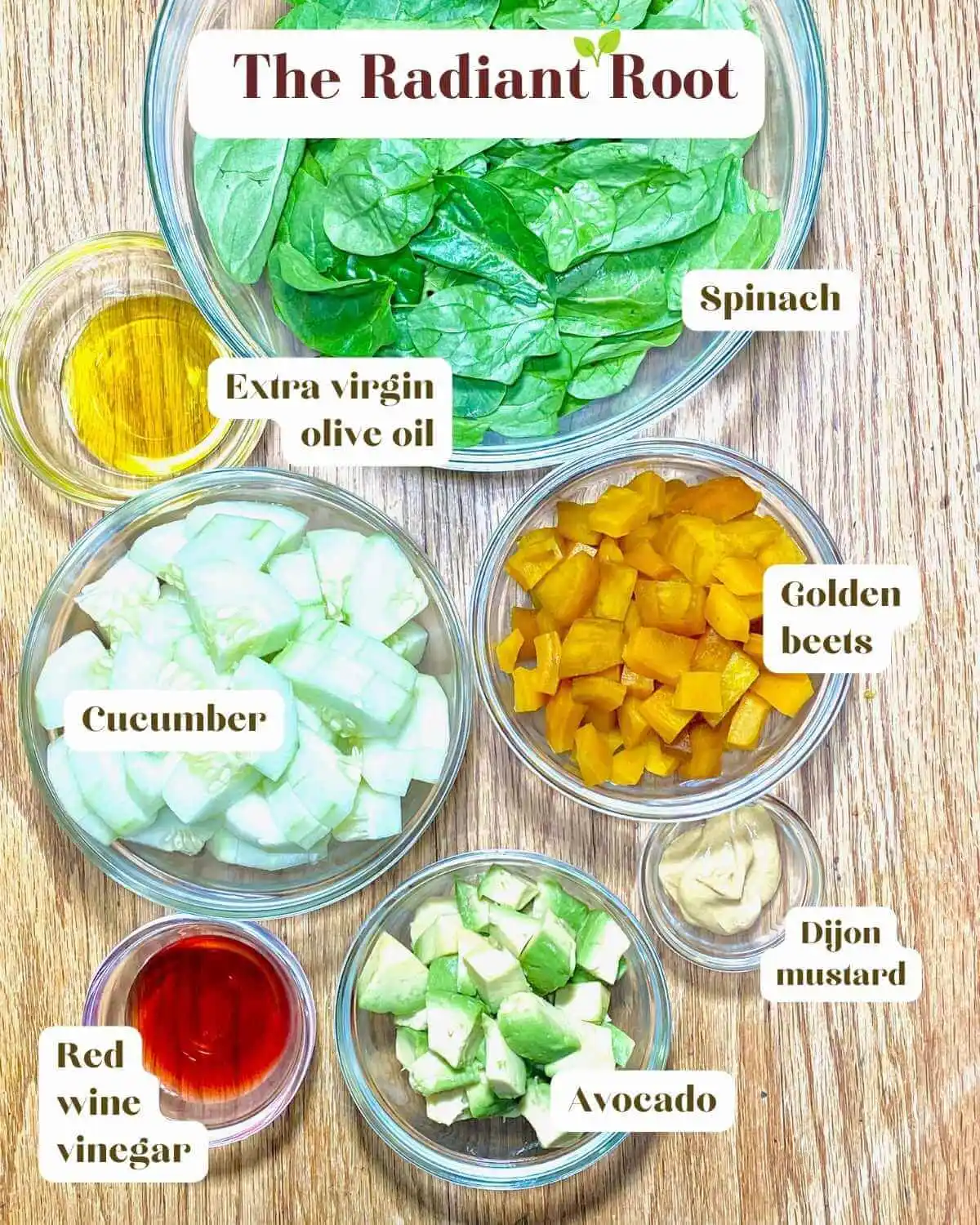 Golden Beet Salad Ingredient photo: A wooden table with the ingredients for golden beet salad in clear glass bowls with the names next to them they include spinach, extra virgin olive oil, cucumbers, red wine vinegar, Dijon mustard, avocado, and golden beets | best ways to eat beets | The Radiant Root