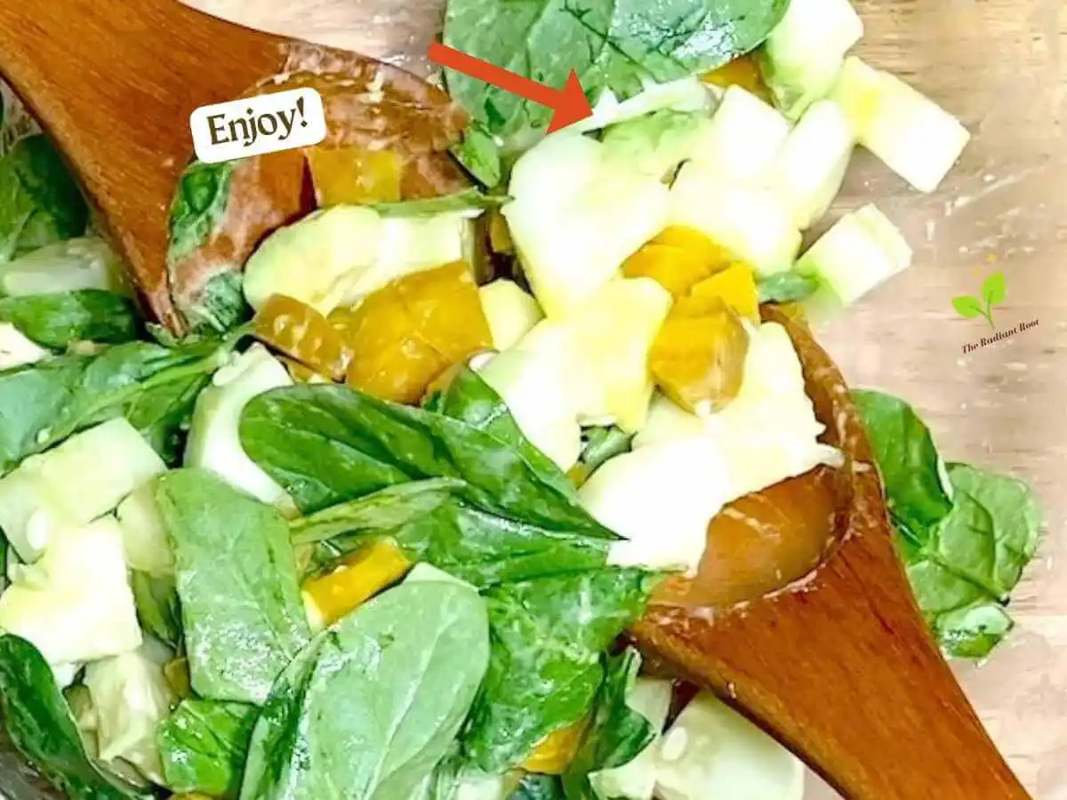 Golden Beet Salad recipe instruction photo 11 of 11 : A wooden table with a close up of a clear medium mixing bowl containing spinach, cucumbers, avocado, cucumber tossed with Dijon dressing, In the bowl are wooden tongs. In the upper left corner it reads “Enjoy!” | how do you cook beets | The Radiant Root