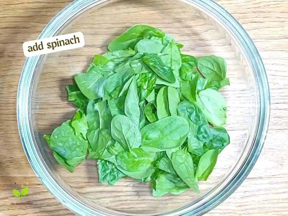 Golden Beet Salad recipe instruction photo 5 of 11 : A wooden table with a close up of a clear medium mixing bowl containing spinach. In the upper left corner it reads “Add spinach.” | Golden beets nutrition | The Radiant Root