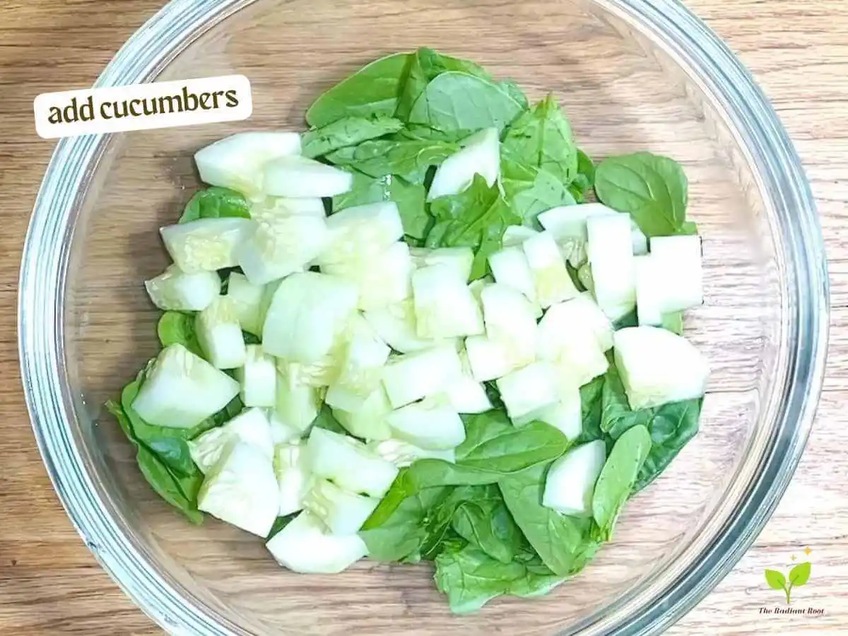 Golden Beet Salad recipe instruction photo 6 of 11 : A wooden table with a close up of a clear medium mixing bowl containing spinach and cucumbers. In the upper left corner it reads “Add cucumbers.” | beets healthy | The Radiant Root