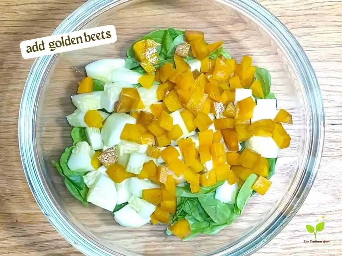 Golden Beet Salad recipe instruction photo 7 of 11 : A wooden table with a close up of a clear medium mixing bowl containing spinach, cucumbers, and beets. In the upper left corner it reads “Add golden beets.” | Red beets vs golden beets | The Radiant Root