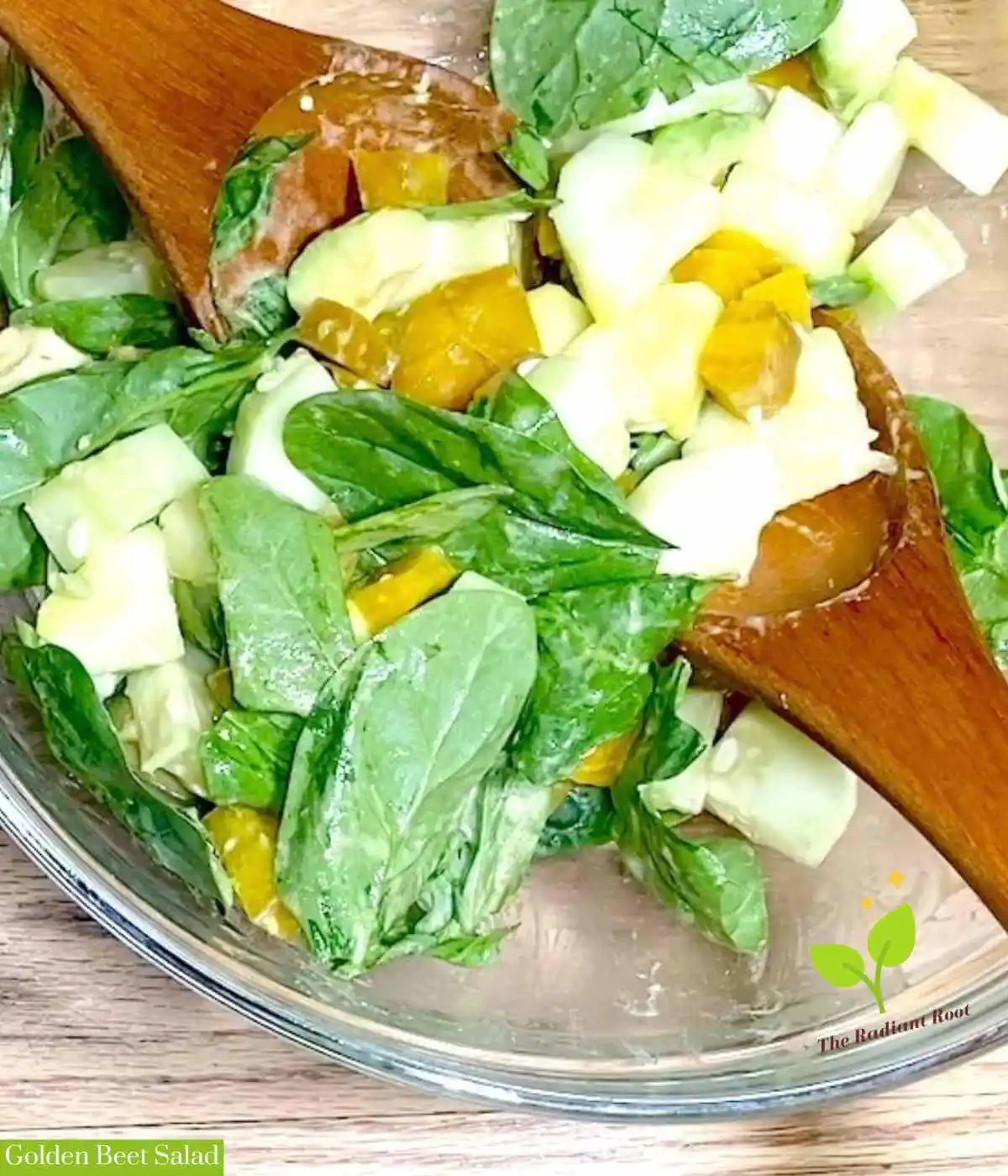 Golden Beet Salad main photo: The close up of a clear glass bowl on a wooden table containing spinach beet salad, cucumber, avocado topped with with a dijon mustard dressing.In the bottom left corner it says “Golden Beet Salad.” | The Radiant Root