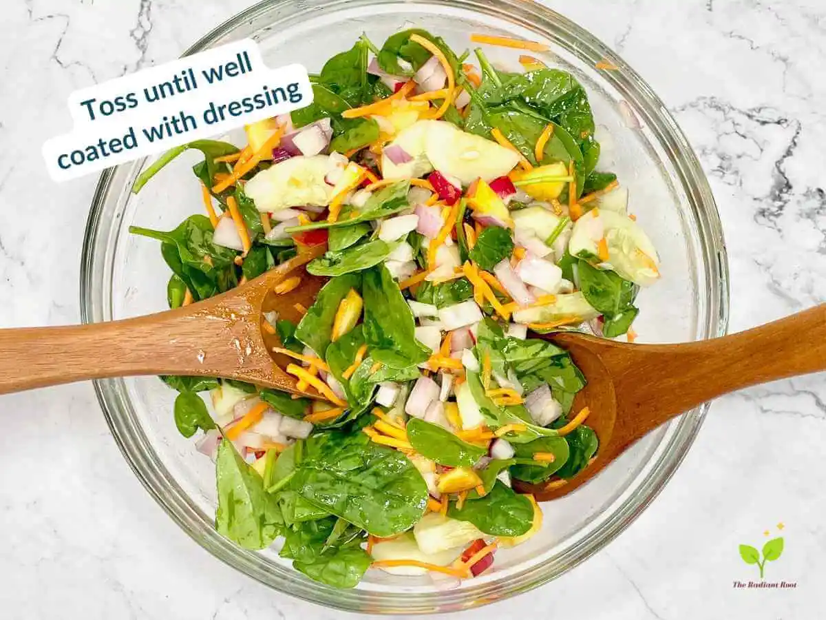 Peach Spinach Salad recipe instruction photo 11 of 12 : A white marble table containing a large clear glass mixing bowl containing spinach, diced red onions, cucumbers, carrots, radishes, and peaches tossed with the extra virgin olive oil and red wine vinegar dressing with salad tongs sitting in the bowl. In the upper left corner it reads “toss until well coated with dressing.” | How to store peach | The Radiant Root