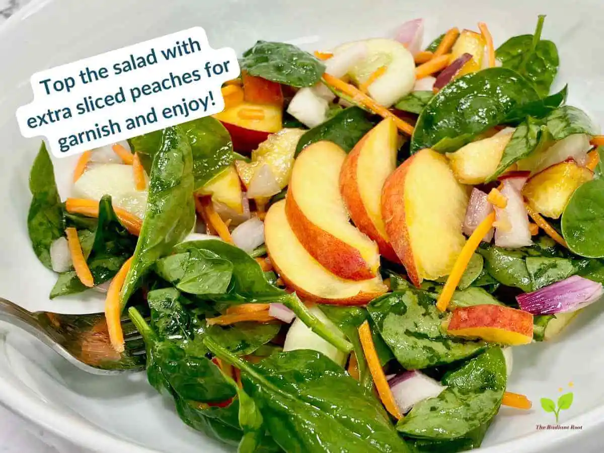 Peach Spinach Salad recipe instruction photo 12 of 12 : A close up of a white marble table containing a large white deep bowl with a finished salad containing peaches, spinach, radishes, cucumber, shredded carrots, and red onion tossed with a red wine vinegar and extra virgin olive oil dressing and topped with sliced peaches as garnish. In the upper left corner it reads “top the salad with extra sliced peach for garnish and enjoy!” | What does peach taste like | The Radiant Root