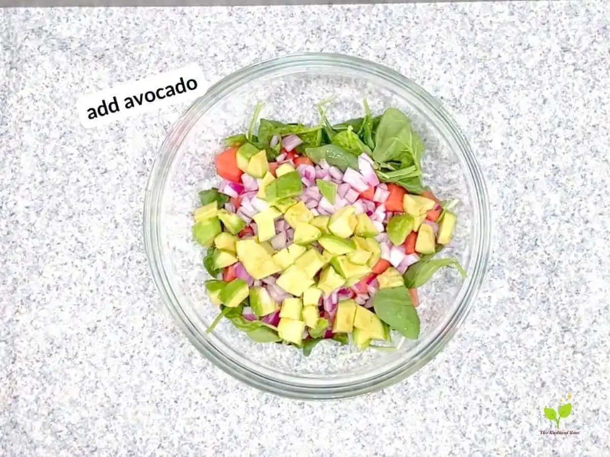 Watermelon avocado salad recipe instruction photo 16 of 20: There is a black speckled table top with a large clear glass mixing bowl on top. Inside the bowl is spinach, watermelon, red onion, and avocado. In the upper left hand corner it reads “add avocado.” | best watermelon | The Radiant Root