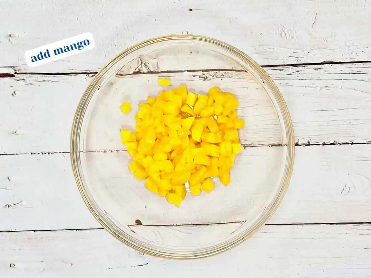 Mango Salsa recipe instruction photo 2 of 7 : A wooden table with a medium clear glass mixing bowl containing diced mango. In the upper left hand corner it reads “add mango.” | how to tell if a mango is ripe | The Radiant Root