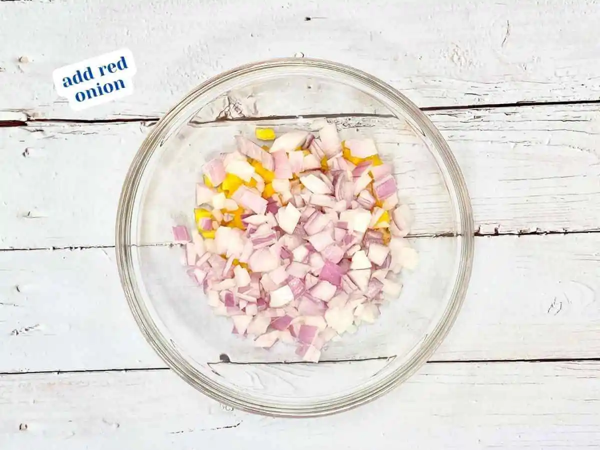 Mango Salsa recipe instruction photo 3 of 7 : A wooden table with a medium clear glass mixing bowl containing diced mango and red onion. In the upper left hand corner it reads “add red onion.” | How do you prepare a mango | The Radiant Root