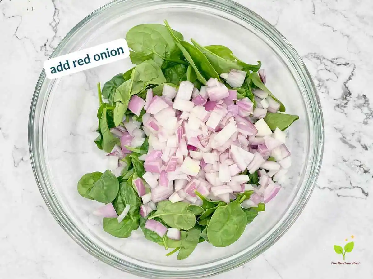 Peach Spinach Salad recipe instruction photo 5 of 12 : A white marble table containing a large clear glass mixing bowl containing spinach and diced red onions. In the upper left corner it reads “add red onion.” | dressing for spinach salad | The Radiant Root