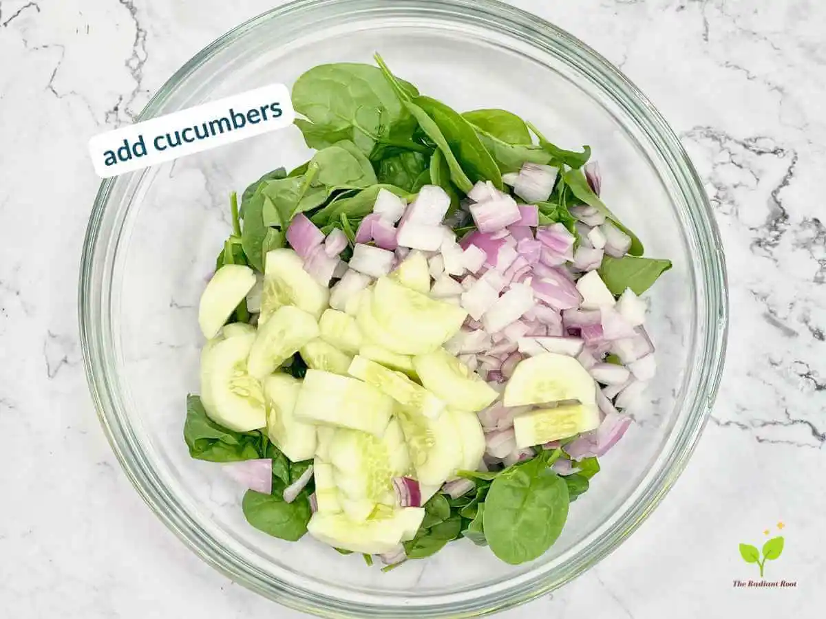 Peach Spinach Salad recipe instruction photo 6 of 12 : A white marble table containing a large clear glass mixing bowl containing spinach, diced red onions, and cucumbers. In the upper left corner it reads “add cucumbers.” | spinach peach salad | The Radiant Root