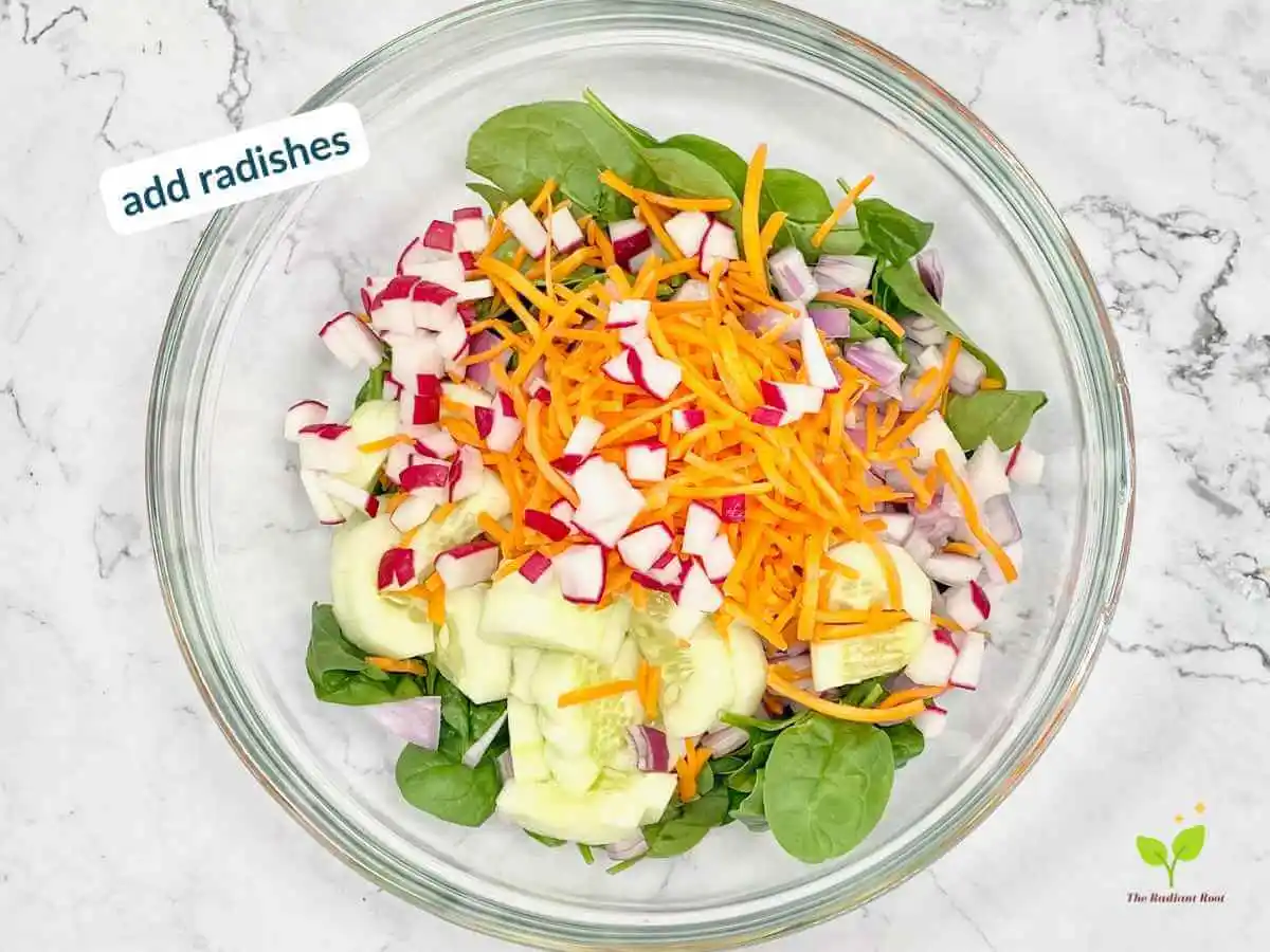 Peach Spinach Salad recipe instruction photo 8 of 12 : A white marble table containing a large clear glass mixing bowl containing spinach, diced red onions, cucumbers, carrots, and radishes. In the upper left corner it reads “add radishes.” | summer salad with peaches | The Radiant Root