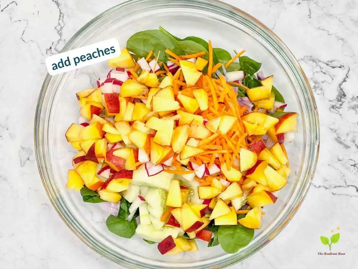 Peach Spinach Salad recipe instruction photo 9 of 12 : A white marble table containing a large clear glass mixing bowl containing spinach, diced red onions, cucumbers, carrots, radishes, and peaches. In the upper left corner it reads “add peaches.” | Salads with fresh peaches | The Radiant Root